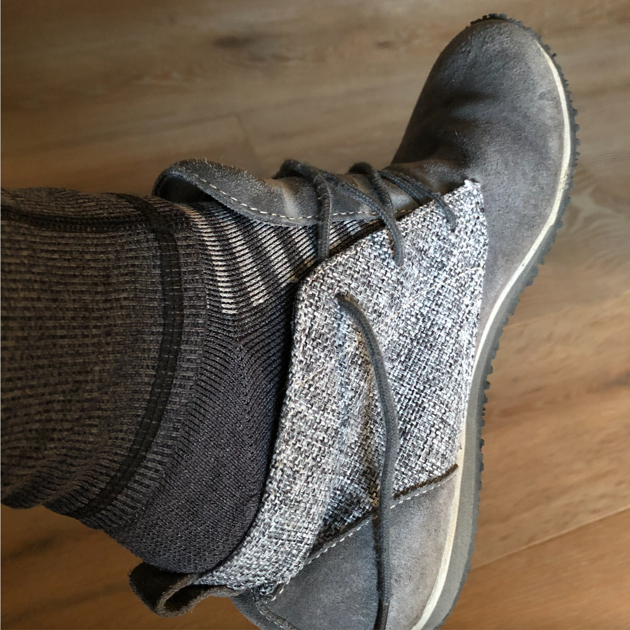 Close up of a grey suede shoe with grey and white striped socks with grey leggings