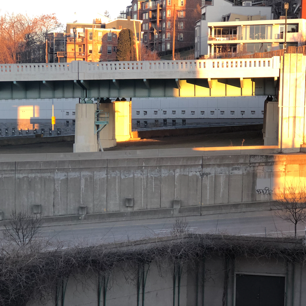 A section of freeway overpasses and ramps, with one pillar glowing golden in the early morning sun
