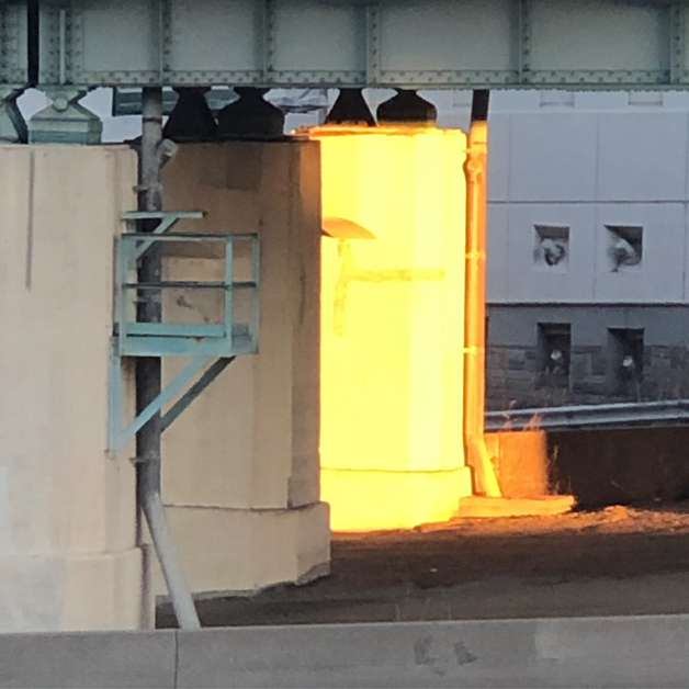 A concrete pillar under an overpass, glowing golden in the early morning sun