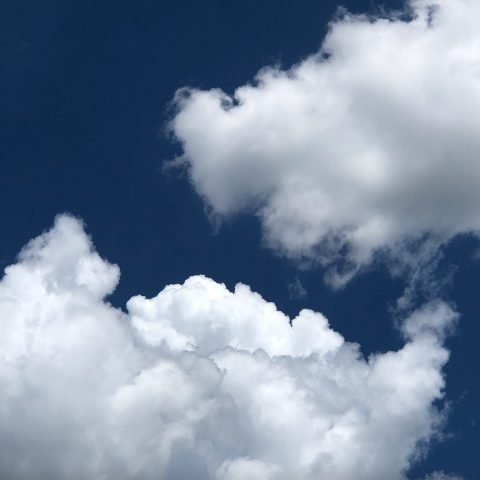 A deep blue sky with two white fluffy clouds meeting in the middle