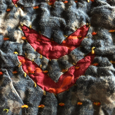 Close-up of a gray quilt with two nested red angles