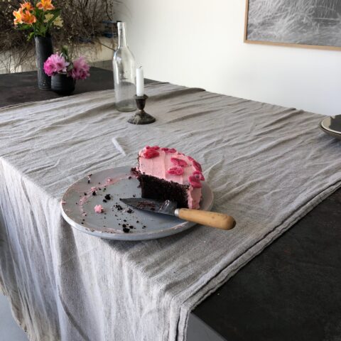 The remains of a chocolate cake with pink icing with red roses on a grey dish and linen tablecloth