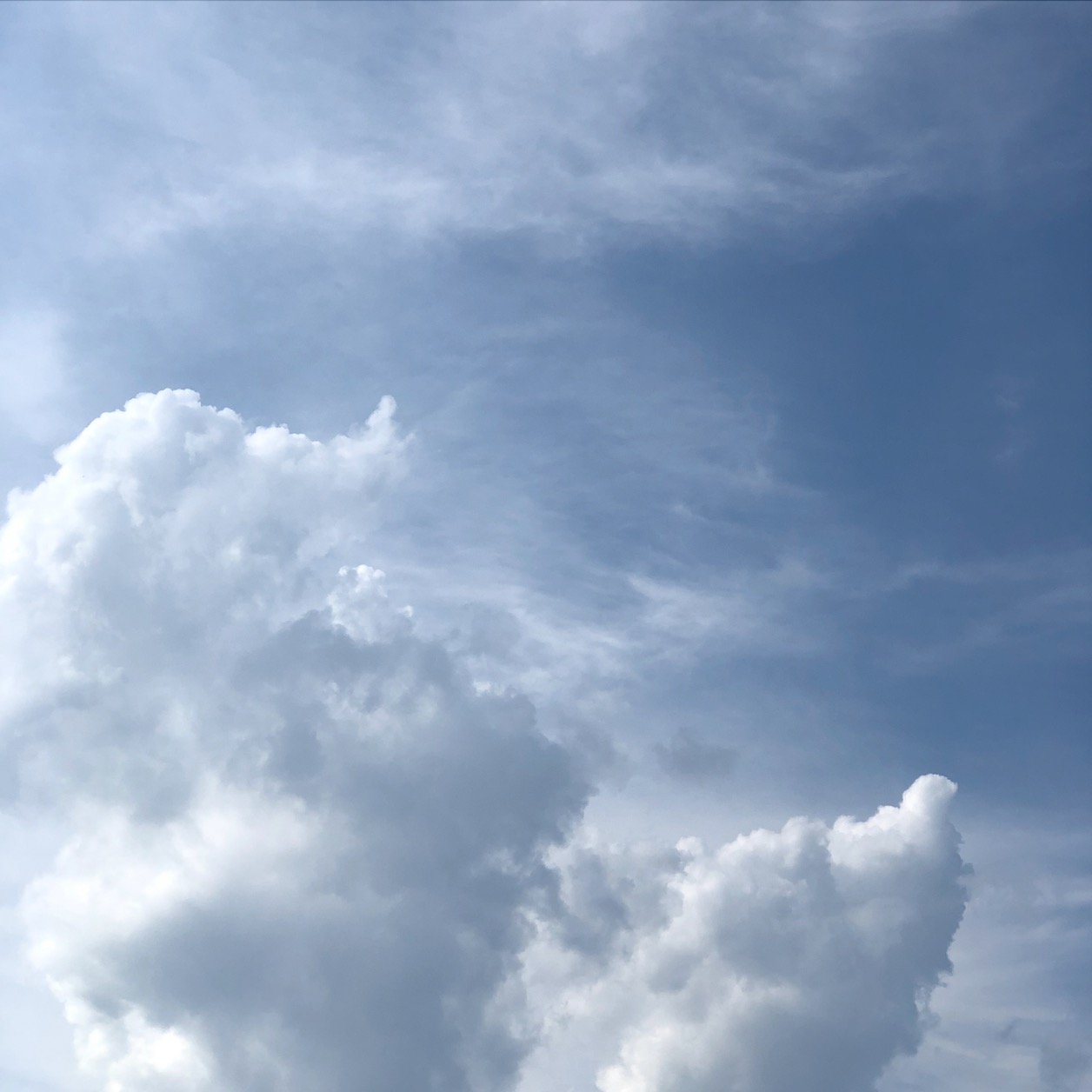 photo of white and gray clouds reaching up on a hazy blue sky