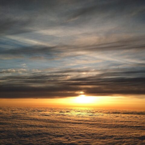sunset in the sky, taken from an airplane, as the sun set between clouds above and below, sending a golden light across the bottom clouds