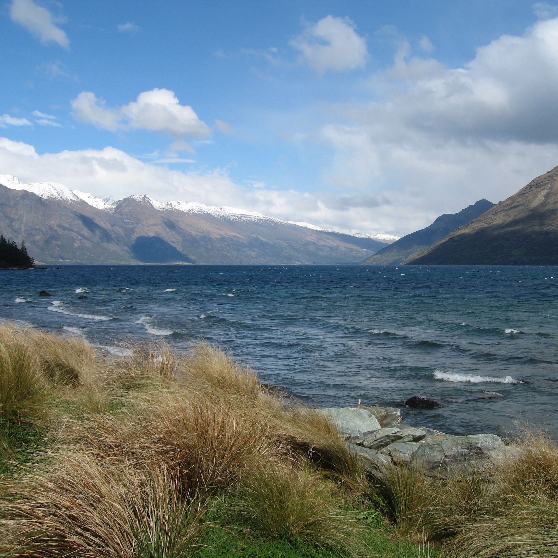 A lake in New Zealand, aquamarine blue, with whitecaps on the water, surrounded by mountains