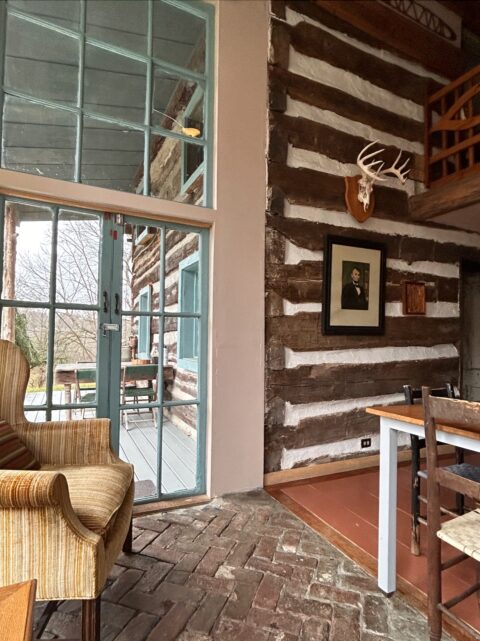 Inside an old log cabin with hand-hewn logs and a floor-to-ceiling stack of windows