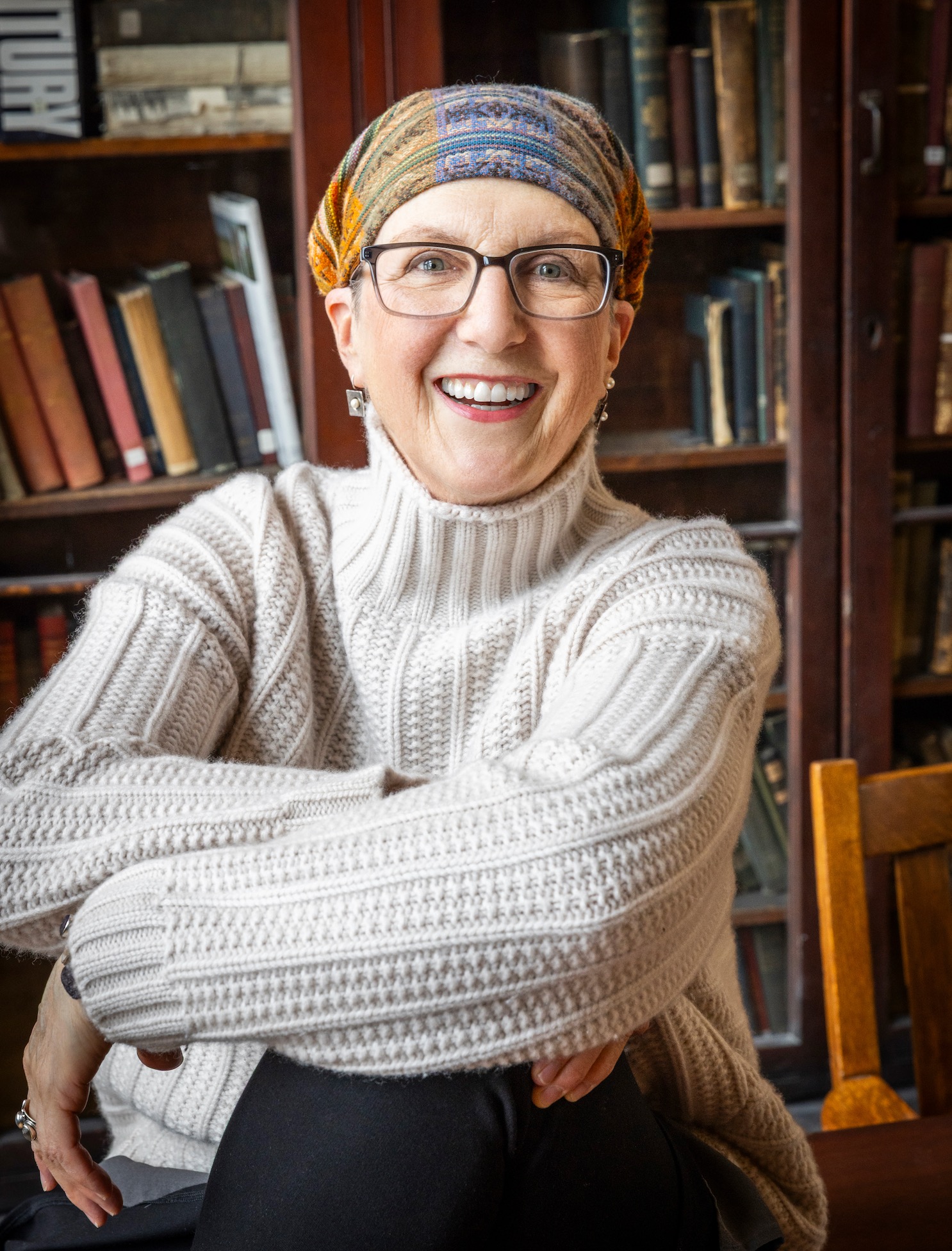 138_WhiteSweaterSeatedonTable_basisforheadshot Jule seated and smiling, with books in the background